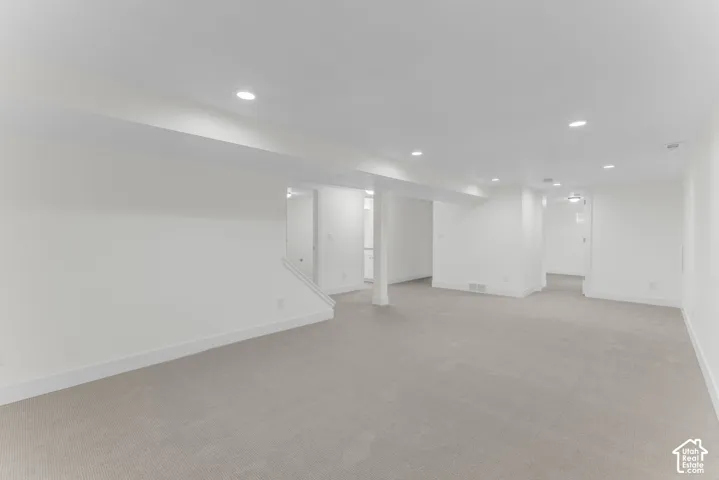 Expansive carpeted area with recessed lighting and a neutral white color palette