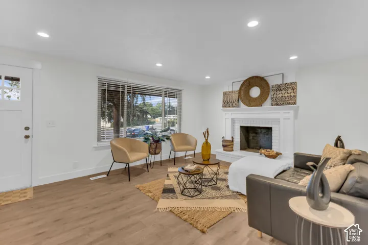 Wood-finish flooring, recessed lighting, substantial front window, white painted brick fireplace with mantel, and a white entry door with glass panels