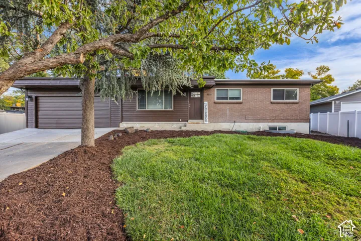 Brick and wood-sided exterior, attached garage, concrete driveway, front lawn, and mature tree