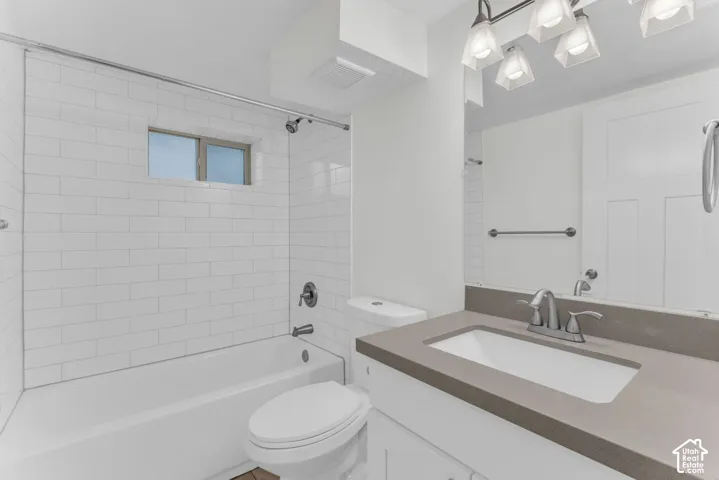 Bathroom featuring a white subway tile tub surround, built-in bathtub, window, vanity with an integrated sink, and overhead lighting