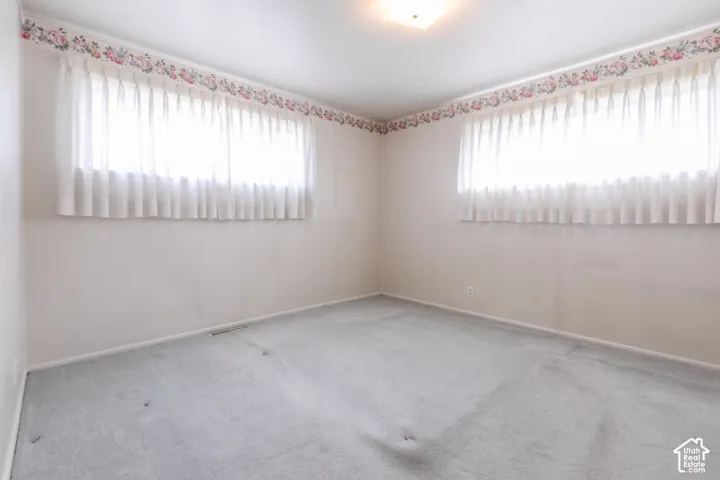 Spacious corner bedroom flooded with natural light through dual windows with vertical blinds and coordinating valances