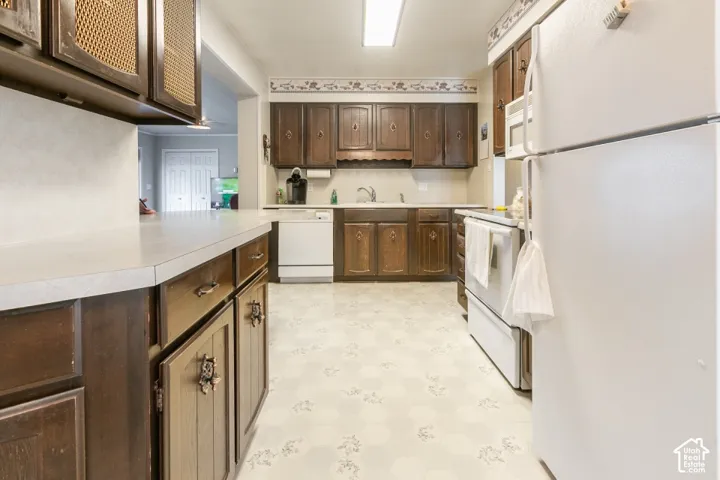 Kitchen featuring dark wood cabinetry, light-toned countertops, integrated white appliances, and patterned flooring