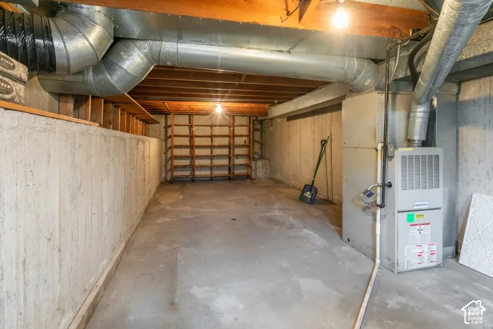 Unfinished basement featuring concrete flooring, exposed wooden ceiling joists, built-in shelving, and utility systems