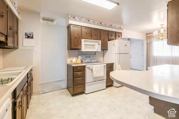 Kitchen featuring wood-finish cabinetry, white appliances, a white sink, and patterned flooring
