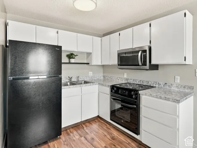 Wood-finish flooring, white cabinetry, stainless steel microwave, black range, and black refrigerator