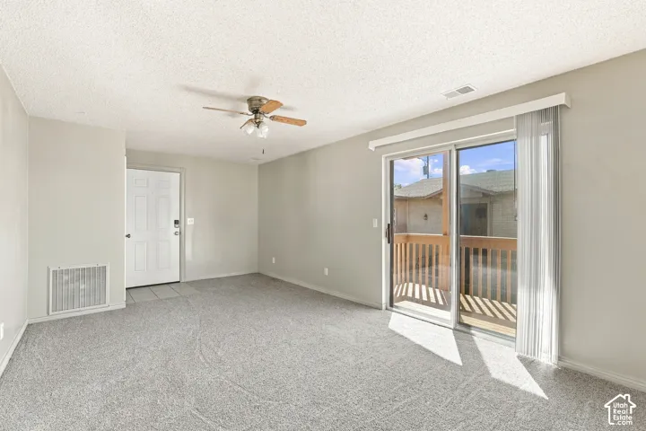 Neutral wall paint, ceiling fan with light fixture, sliding glass door, patio with wood railing, and gray carpeting