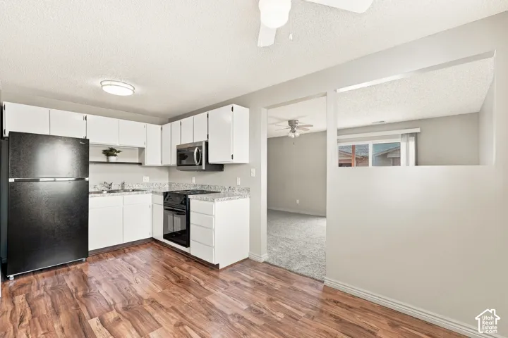 Kitchen featuring wood-finish flooring, white cabinetry, a black refrigerator, a black range, and light-toned countertops