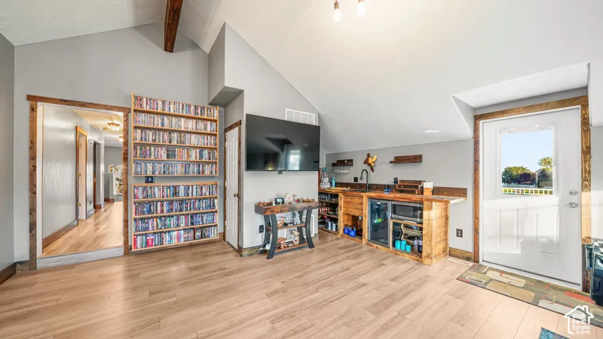 Vaulted ceiling with exposed wood beams, wood-finish flooring, built-in shelving, and a wet bar with integrated appliances