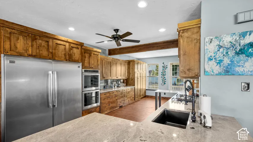 Kitchen featuring stainless steel refrigerator, double wall ovens, wood cabinetry, granite-finish countertops, and an undermount sink with a matte black faucet