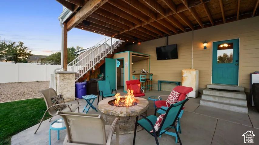Concrete patio with a built-in stone fire pit, covered outdoor area with exposed wood beams, and a concrete staircase