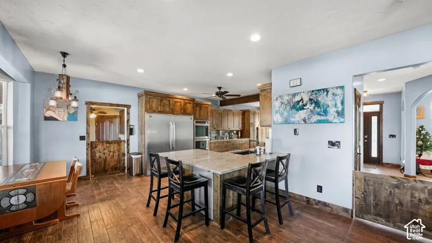 Expansive kitchen featuring wood-finish flooring, light wood cabinetry, stainless steel appliances, a light-toned island with a sink, and recessed lighting