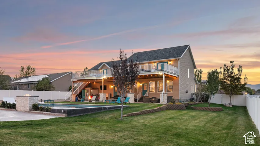 Expansive backyard with a manicured lawn, an in-ground swimming pool, a stone fire pit, a covered patio, and a second-story deck with glass railings