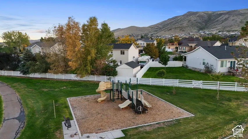 Expansive green space featuring a playground, paved pathway, and white fencing
