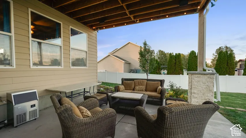 Covered concrete patio featuring an exposed rafter ceiling, string lighting, and a stone-clad support column