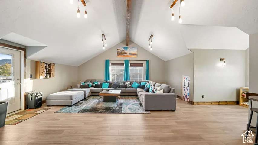 Vaulted ceiling with exposed wood beam, wood-finish flooring, recessed windows, and mounted light fixtures