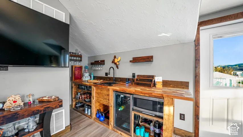 Built-in beverage bar with wood-finish countertop, dark wood-finish cabinetry, under-counter refrigerator, and a stainless steel microwave