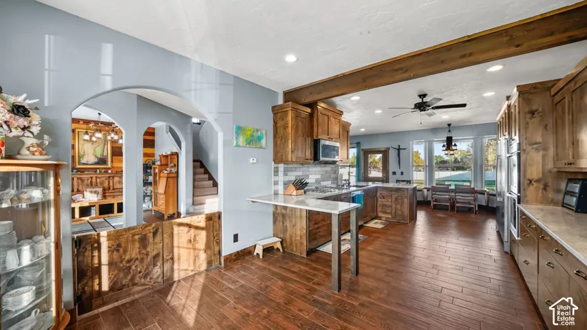 Spacious kitchen featuring warm wood-finish flooring, custom wood cabinetry, stainless steel appliances, and a tiled backsplash