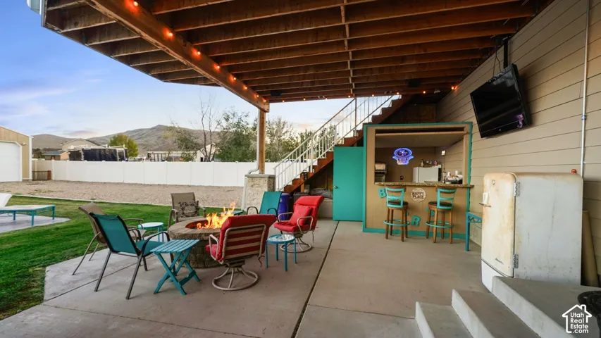 Covered concrete patio with exposed wood ceiling, built-in outdoor bar, and stone fire pit