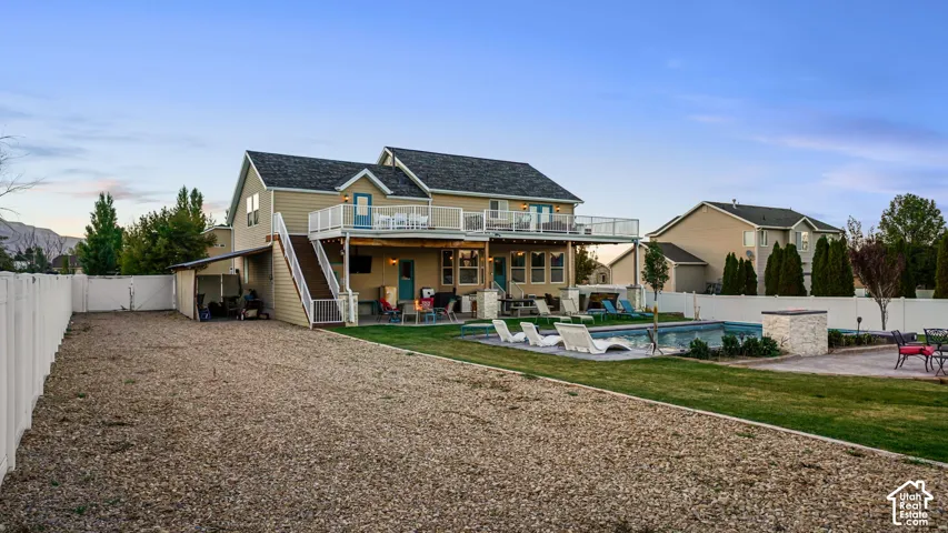 Two-story exterior with a second-level balcony, ground-level covered patio, and fenced backyard with a pool
