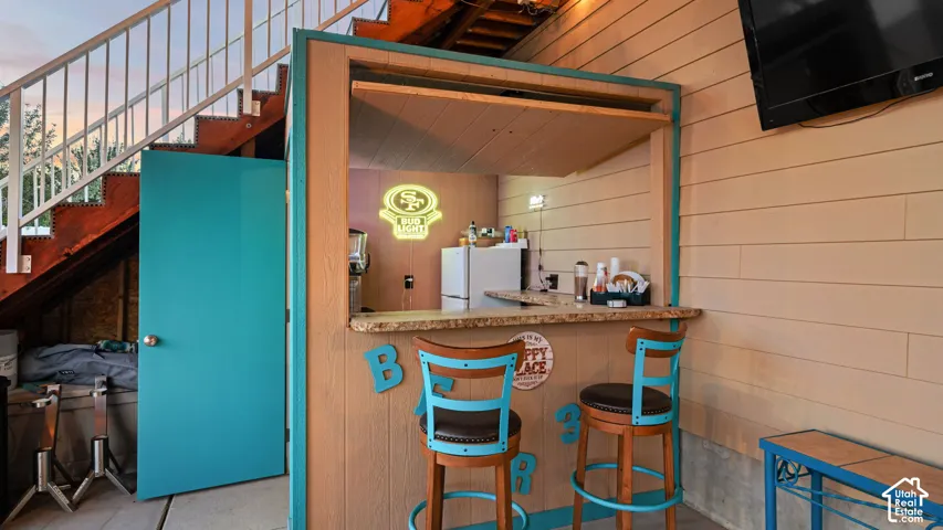 Outdoor bar with a stone-finish countertop, a mounted television, and a wood-paneled exterior