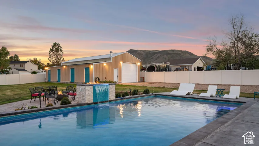 Expansive backyard featuring a large swimming pool with decorative tile, a waterfall feature, and a paved patio area