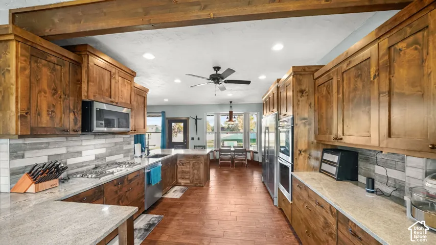 Kitchen featuring wood-finish cabinetry, stainless steel appliances, granite countertops, wood-finish flooring, and a decorative tile backsplash