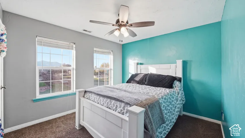 Carpeted bedroom featuring multiple windows, a ceiling fan with integrated lighting, and painted walls