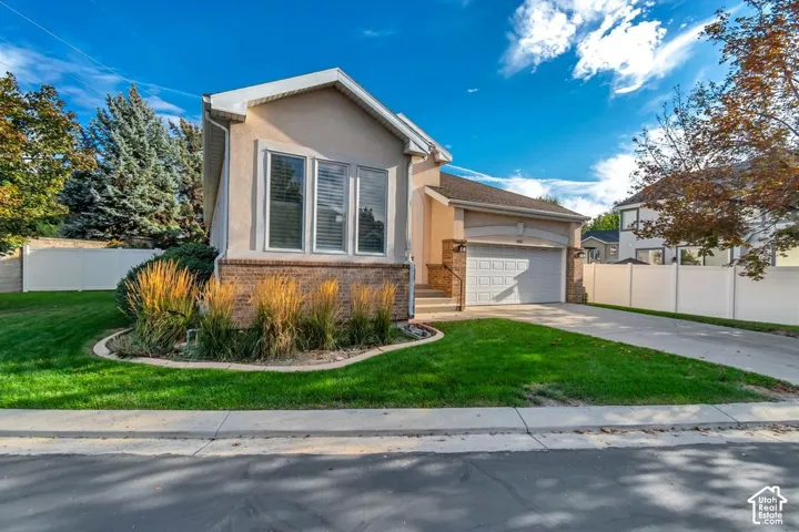 Stucco exterior with a brick-clad foundation, mature landscaping, a two-car garage, and a concrete driveway