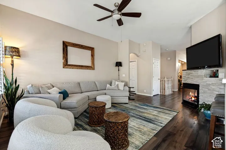 Living area featuring wood-finish flooring, a ceiling fan, and a fireplace with a stone surround