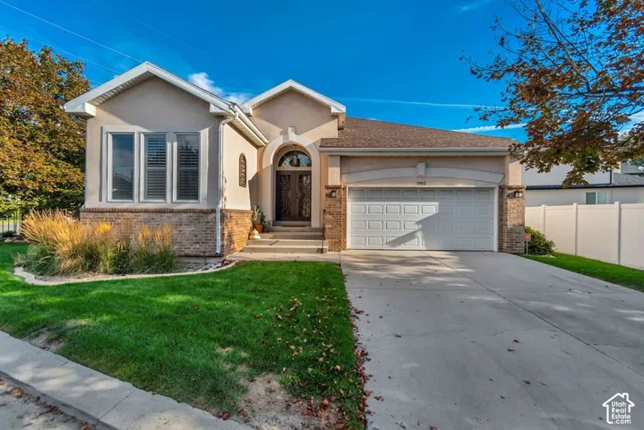 Stucco and brick exterior with a concrete driveway, an arched entry, a two-car garage, and a manicured lawn