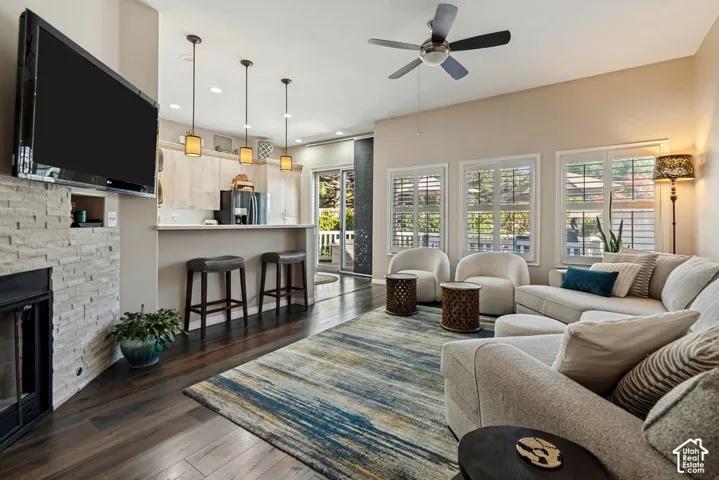 Hardwood flooring throughout, stacked stone fireplace, multiple windows with white shutters, ceiling fan, and recessed lighting