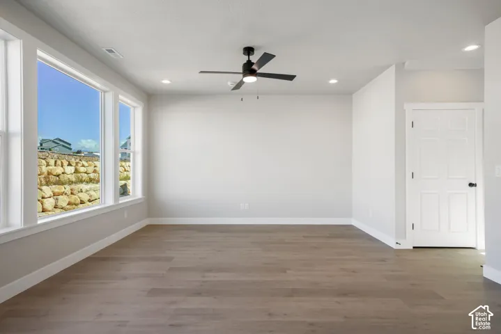 Wood-finish flooring, multiple large windows, recessed lighting, ceiling fan, and white paneled door