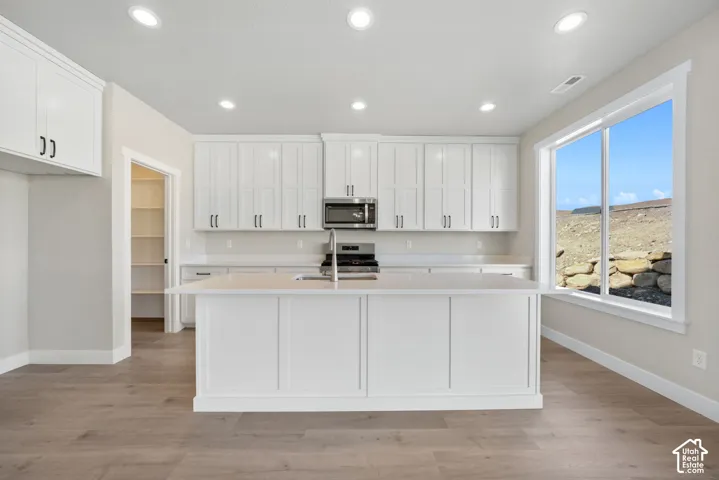 Contemporary kitchen featuring white shaker-style cabinetry, stainless steel appliances, quartz countertops, a large center island with seating space, and abundant natural light from expansive windows overlooking the surrounding landscape