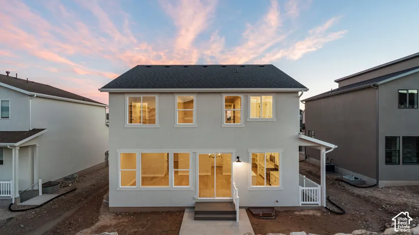 Two-story stucco exterior featuring a dark shingle roof, white trim windows, and a sliding glass door with an adjacent exterior light fixture