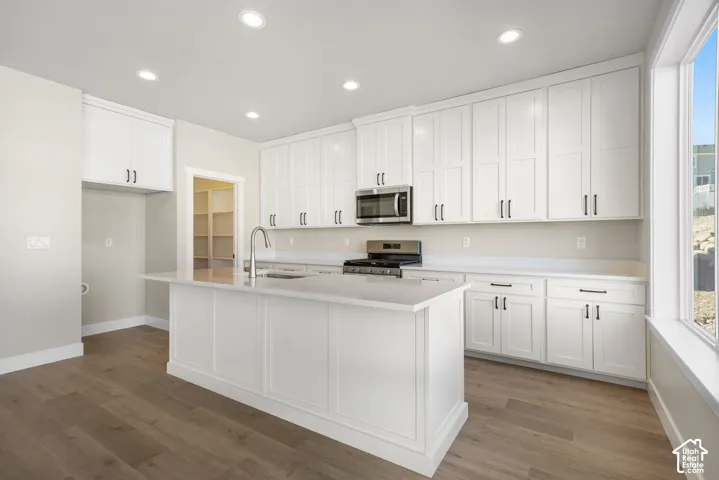 Kitchen featuring white shaker cabinetry, stainless steel microwave and range, light-toned countertops, and wood-finish flooring