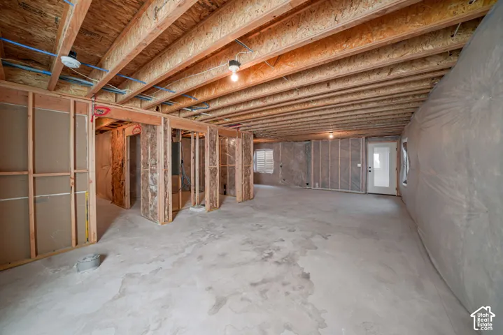 Unfinished basement with exposed wood framing, concrete flooring, and an exterior door with a window pane