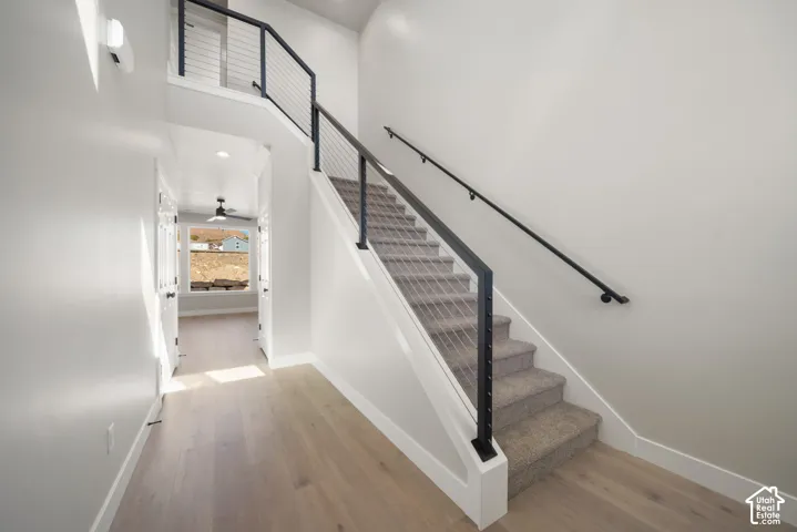 Wood-finish flooring leading to a carpeted staircase with a modern cable railing system and dark handrail