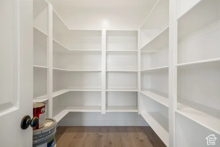Walk-in pantry featuring extensive white shelving, wood-finish flooring, and a white interior door with a matte black doorknob