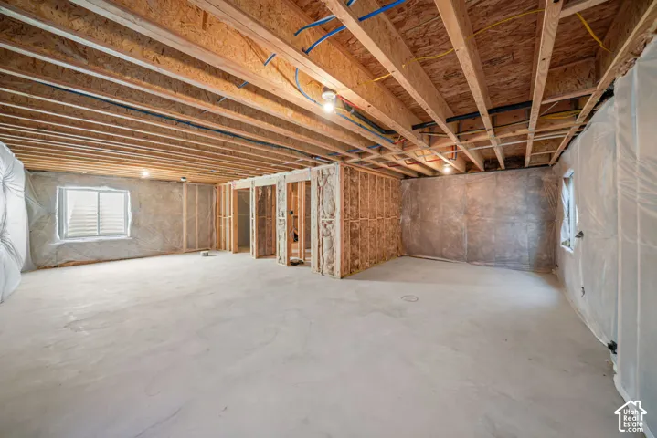 Unfinished basement with exposed ceiling joists, concrete flooring, framed wall sections, and multiple windows