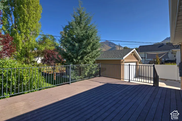 Expansive composite decking with black metal railing, featuring a detached garage, mature trees, and a distant mountain backdrop