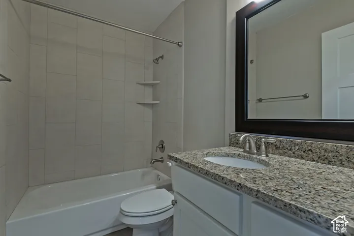 Bathroom featuring a white bathtub, tiled shower surround, recessed shelving, a vanity with a granite-style countertop, and a framed mirror