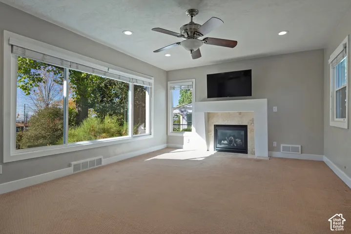 Recessed lighting, wood-finish ceiling fan, fireplace with a stone surround and mantel, and large picture windows