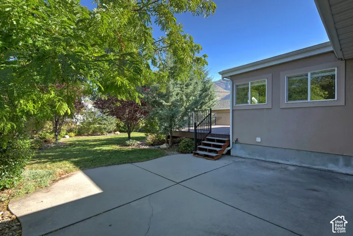 Expansive concrete patio with direct access to a raised deck featuring stairs and dark railings