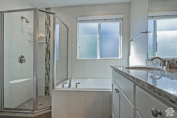 Shower enclosure with a built-in bench, tiled walls, a soaking tub, a window with privacy glass, and a vanity featuring a granite countertop