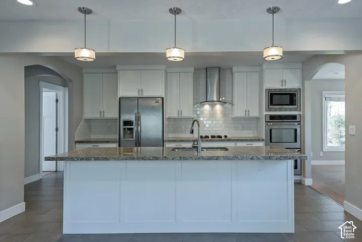 Spacious kitchen featuring white cabinetry, a large center island with a granite countertop, stainless steel appliances, and a subway tile backsplash