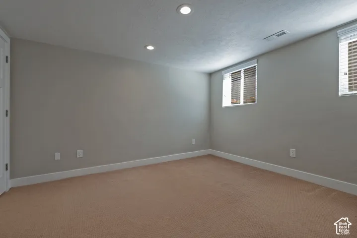Recessed lighting, neutral wall paint, two windows with blinds, light-colored carpeting, and white trim