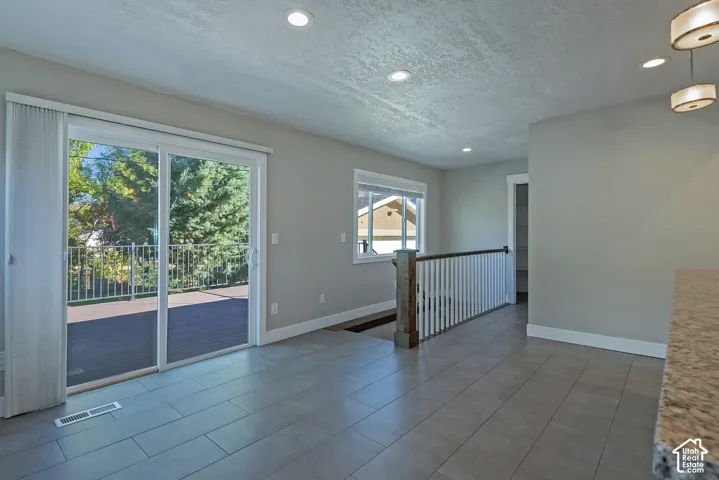 Sliding glass patio doors to exterior deck, recessed ceiling lighting, light grey wall paint, wood-finish and white staircase railing, and tile flooring