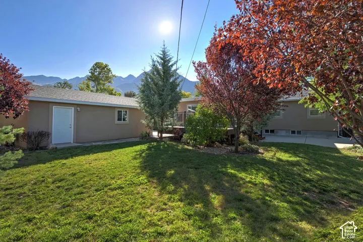 Expansive grassy yard with mature trees, stucco exterior, and mountain scenery