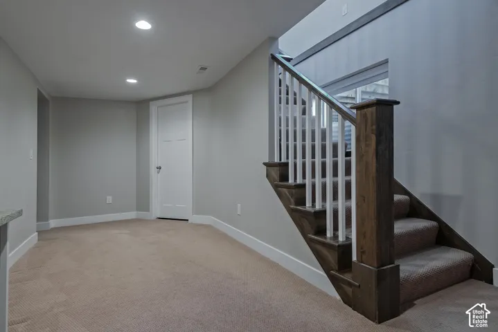 Carpeted flooring, recessed lighting, white interior door with paneling, and wood-finish stair railing with white balusters