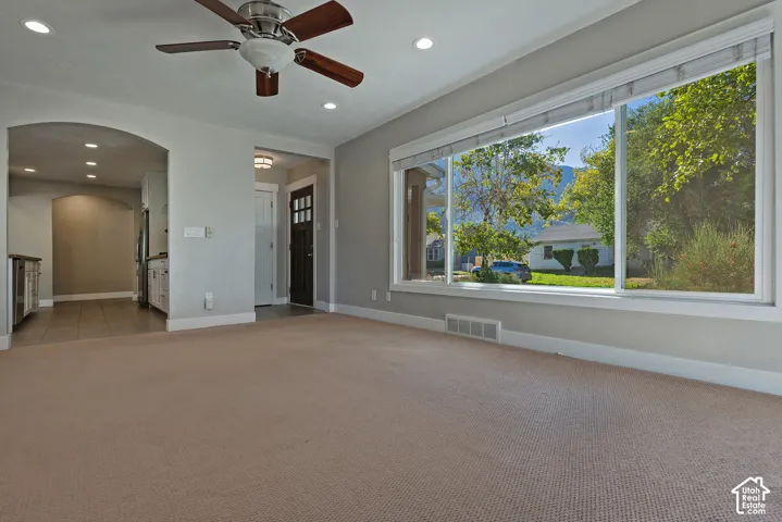 Expansive picture window, recessed ceiling lighting, ceiling fan, arched doorway, and dark wood-finish entry door